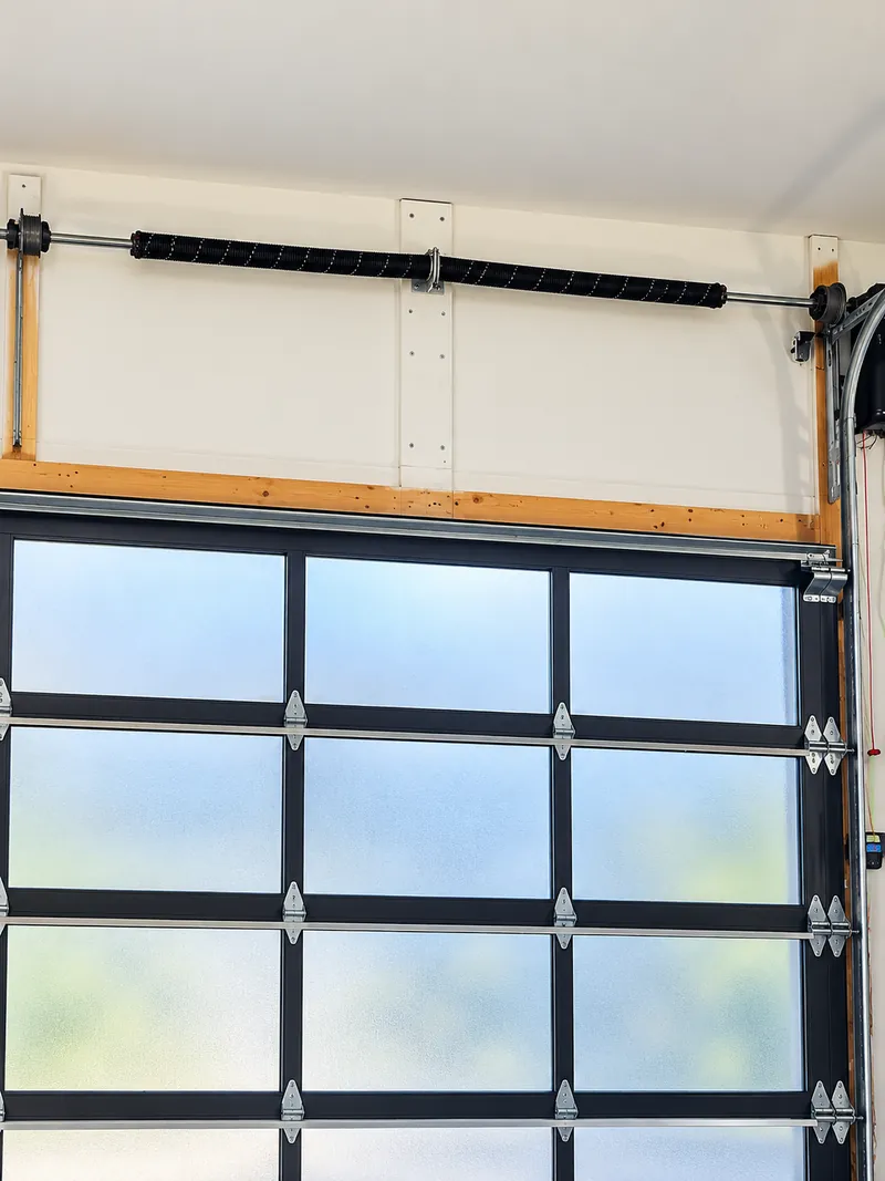 Garage door torsion spring assembly above a glass panel garage door